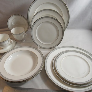 May include: A set of white porcelain dinnerware with a silver and gold geometric pattern. The set includes a large dinner plate, a salad plate, a soup bowl, a bread and butter plate, a teacup, and a saucer.