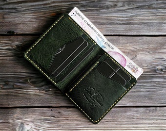 Puede incluir: Una cartera de cuero verde oscuro con detalles de costura amarilla. La cartera está abierta y tiene múltiples ranuras para tarjetas y un compartimento para billetes. Un billete de lira turca es visible dentro de la cartera.