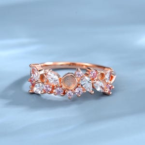 May include: Rose gold ring featuring a floral design with clear and pink gemstones. The ring has a delicate, nature-inspired aesthetic, with a band adorned with various shapes of stones.