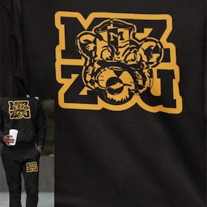 May include: A black long-sleeved sweatshirt and matching black jogging bottoms featuring a yellow graphic print of a tiger mascot head centred within the block letters MIZ ZOU. The design includes a stylised letter M on the tiger's forehead.