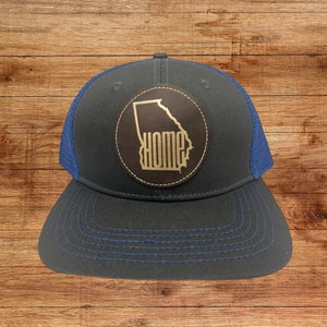 May include: A black and blue trucker hat with a brown leather patch featuring the outline of the state of Georgia and the word "HOME" in gold lettering.