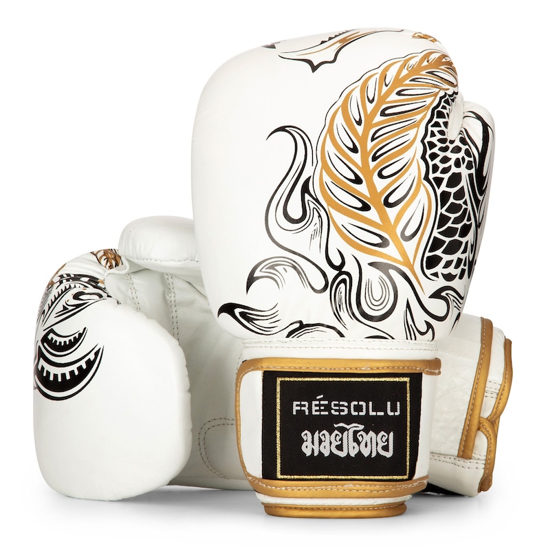 May include: White leather boxing gloves with a black and gold koi fish design. The gloves have a black patch with the text "FREESOL.U" and "มวยไทย" in Thai.