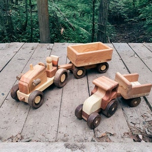 May include: Three wooden toy tractors with trailers. The tractors are brown and natural wood with black wheels. The trailers are brown wood with no wheels. The toys are on a wooden surface.