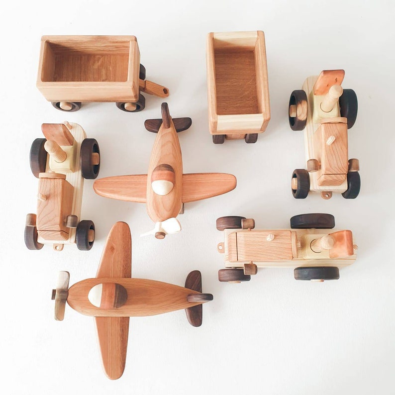 May include: A set of wooden toy vehicles, including a tractor, a truck, a plane, and a wagon. The toys are made of natural wood and have a rustic, handmade look.