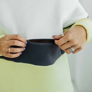May include: A white, grey, and yellow striped sweatshirt with a zipped pocket on the front.