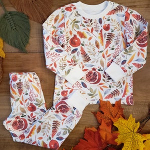 May include: A white long-sleeved shirt and matching trousers with a autumnal print of leaves, pomegranates, and berries.