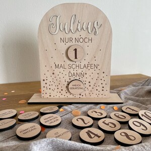 May include: A wooden countdown calendar with a gold glitter background. The calendar says "Julius Nur Noch" and has a number 1 on it. The calendar also says "Mal Schlafen Dann" and "Hab Ich Geburtstag". There are 10 wooden circles with numbers 1 through 10 on them.