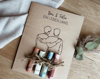 May include: A wooden card with a drawing of two people hugging. The card says "Ben & Felix Ein Leben Lang" and has rolled up bills tied with twine.
