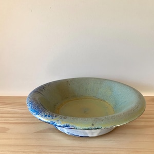 May include: A ceramic bowl with a light blue and green glaze. The bowl has a rounded shape and a slightly raised rim.