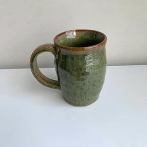 May include: A green ceramic mug with a brown rim and a speckled glaze. The mug has a rounded body and a handle.