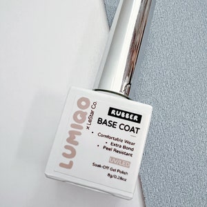 May include: A white bottle of Lumigo x LeStar Co. Rubber Base Coat nail polish. The bottle is labeled with the product name, brand, and size: 8g/0.28oz. The bottle is on a gray surface.