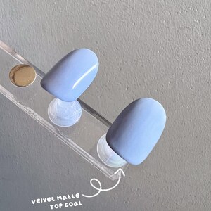 May include: Two light blue nail tips with a velvet matte top coat. The nail tips are displayed on a clear plastic stand.