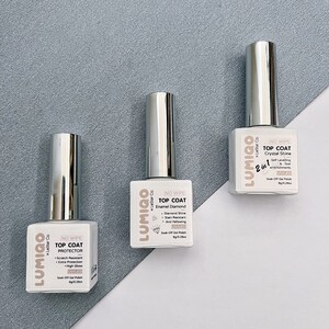 May include: Three bottles of clear nail polish with silver caps. Each bottle has a white label with the brand name "LUMIGO" and the text "NO WIPE TOP COAT" followed by the type of top coat: "PROTECTOR", "Enamel Diamond", and "Crystal Shine".