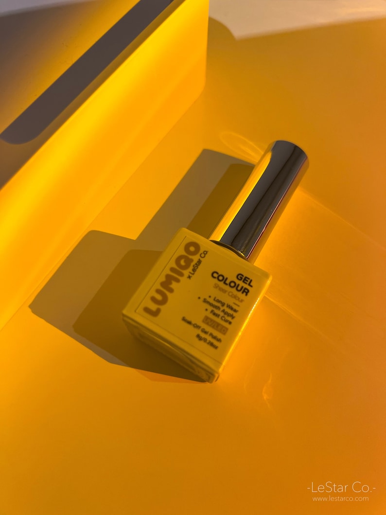 May include: A yellow bottle of Lumigo Gel Colour nail polish with the text "Gel Colour Sheer Colour" and a list of features: Long Wear, Smooth Apply, Fast Cure, Soak-Off Gel Polish. The bottle is on a yellow surface.
