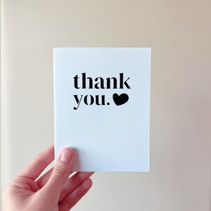 May include: A white card with the text "thank you." in black with a black heart symbol.