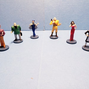 May include: Set of six miniature figurines, each depicting a different character. The figurines are painted in various colors, including red, blue, green, yellow, and white. They are standing on small, round bases.