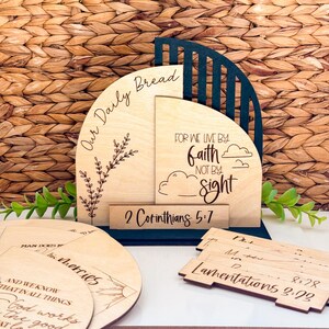 Puede incluir: Decoración religiosa de madera con el texto "Our Daily Bread" y "For we live by faith, not by sight." Incluye piezas de madera adicionales con versículos bíblicos. La pieza principal tiene un acento azul oscuro.