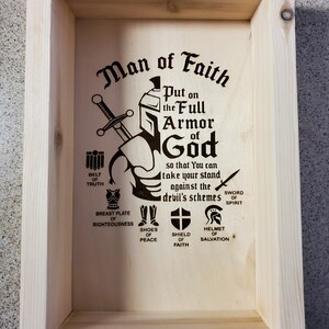 Puede incluir: Una caja de madera con un diseño grabado con láser de un caballero con armadura con el texto "Man of Faith" y "Put on the Full Armor of God so that You can take your stand against the devil's schemes". El diseño incluye una espada, un casco, un escudo, una coraza, un cinturón, zapatos y un casco.