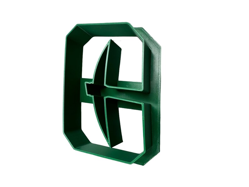 May include: A green plastic cookie cutter shaped like a letter "B" with a curved design in the center.
