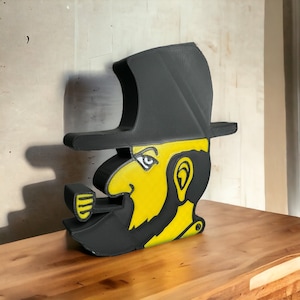 Könnte beinhalten: Eine schwarz-gelbe 3D-gedruckte Figur eines Mannes mit Hut und Pfeife. Der Mann hat ein gelbes Gesicht und einen Bart, und der Hut ist schwarz.
