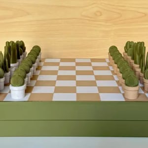 Puede incluir: Un tablero de ajedrez verde y marr&oacute;n con piezas de ajedrez en forma de plantas verdes. El tablero est&aacute; cerrado y las piezas est&aacute;n dispuestas en posici&oacute;n inicial.