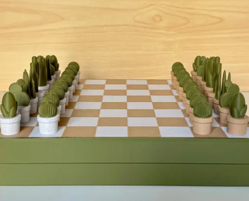 Puede incluir: Un tablero de ajedrez verde y marr&oacute;n con piezas de ajedrez en forma de plantas verdes. El tablero est&aacute; cerrado y las piezas est&aacute;n dispuestas en posici&oacute;n inicial.