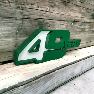 May include: Green and white 3D number 49ers sign. The sign is made of a thick, rigid material and has a white background with green lettering.