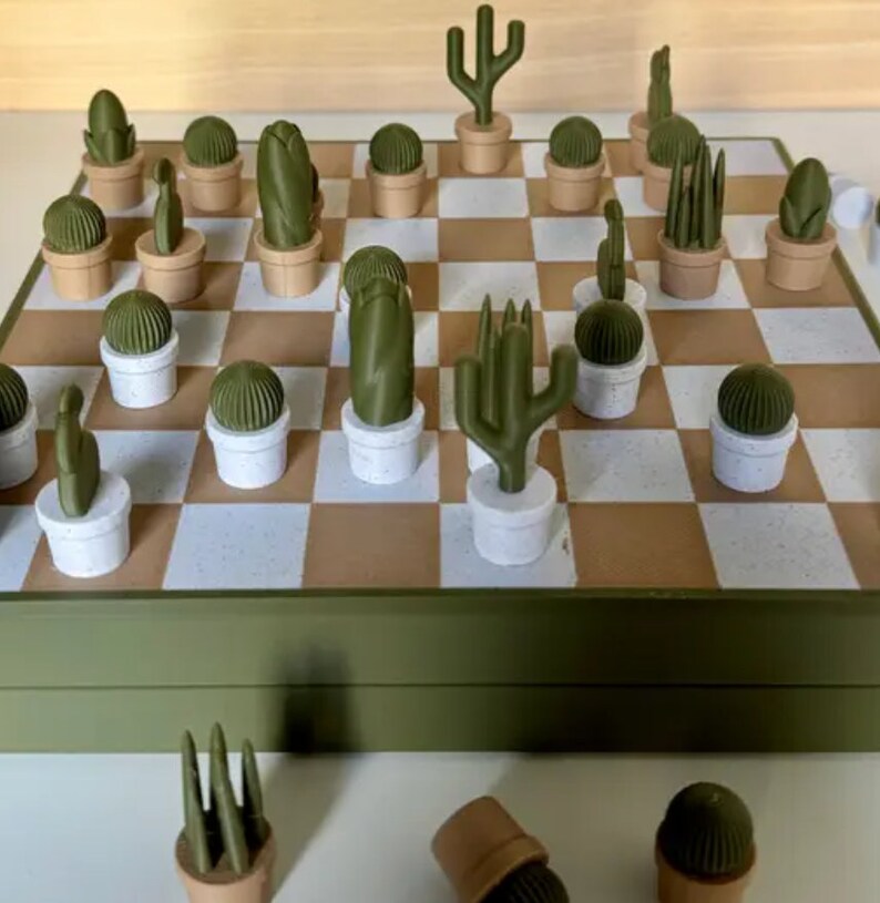 Puede incluir: Un juego de ajedrez verde y marr&oacute;n con piezas con forma de cactus. El tablero est&aacute; cerrado y las piezas est&aacute;n esparcidas a su alrededor.