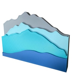 Puede incluir: Una escultura de pared en capas con un diseño de cordillera. La escultura está hecha de papel azul, turquesa y gris y tiene un efecto 3D.