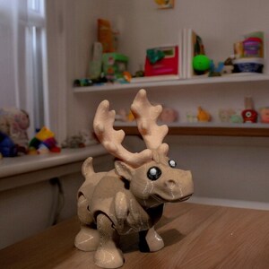 May include: A light brown toy reindeer with large, white eyes and antlers. The reindeer is made of plastic and has a textured surface.