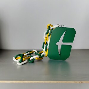 May include: A green and yellow chain necklace with a green pendant featuring a white bird design. The pendant has a cut-out shape and the text "C" in white.