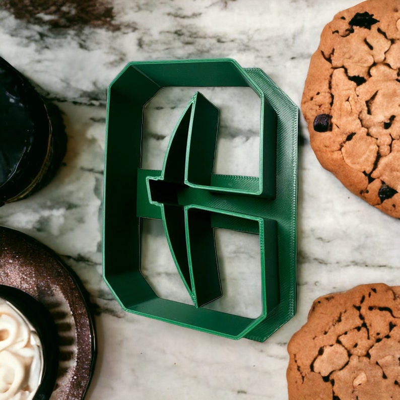 May include: Green plastic cookie cutter shaped like a pickaxe. The cutter is on a marble surface.