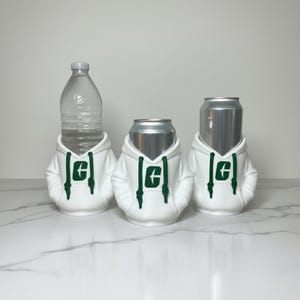 Puede incluir: Tres recipientes para bebidas: una botella de agua y dos latas de aluminio, cada una vestida con una sudadera con capucha blanca con un logotipo verde. Las sudaderas tienen cordones y est&aacute;n dise&ntilde;adas para ajustarse perfectamente a los recipientes.