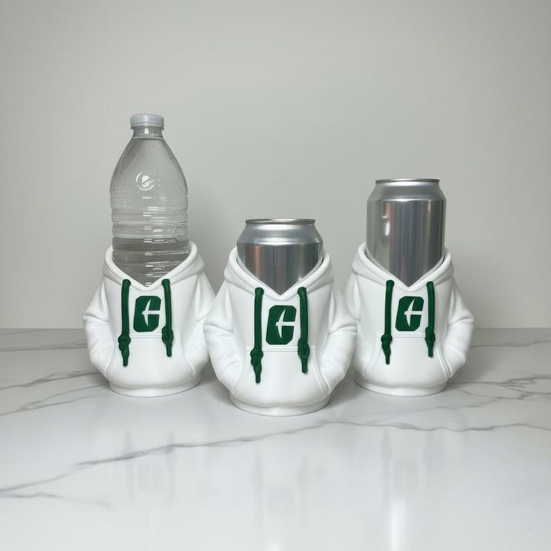 Puede incluir: Tres recipientes para bebidas: una botella de agua y dos latas de aluminio, cada una vestida con una sudadera con capucha blanca con un logotipo verde. Las sudaderas tienen cordones y est&aacute;n dise&ntilde;adas para ajustarse perfectamente a los recipientes.