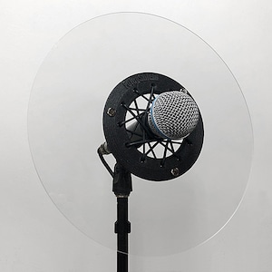 May include: A black microphone with a black pop filter and a clear acrylic shield. The microphone is mounted on a black stand.