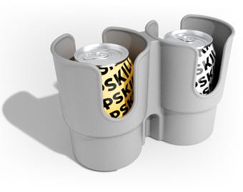 Könnte beinhalten: Ein grauer Doppel-Becherhalter für das Auto mit zwei Aluminiumdosen. Die Dosen haben ein schwarz-weißes Muster. Der Becherhalter besteht aus einem glatten, matten Material und ist für die Konsole eines Autos konzipiert.