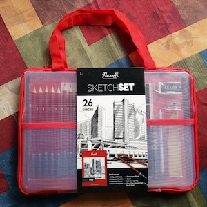 May include: A red zippered sketch set carrying case with a red handle. The case contains pencils, an eraser, and other drawing supplies. The front of the case has a black label that reads "Sketch Set" and "26 pieces."