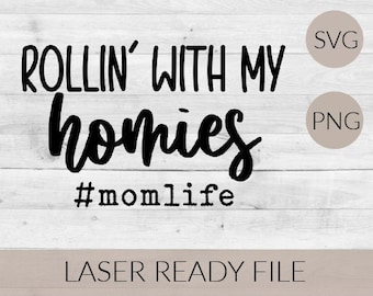 May include: Black and white graphic text on a woodgrain background that reads "Rollin' with my homies #momlife". The text is in a handwritten font. The image also includes the words "SVG" and "PNG" in white circles on a beige background.