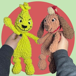 May include: Two crocheted plush toys, one green and one brown. The green toy is shaped like a Grinch with a mischievous expression. The brown toy is shaped like a dog with a red hat and a green collar.