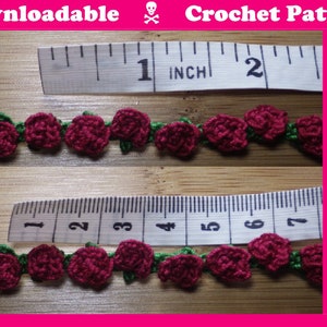 Könnte beinhalten: Nahaufnahme einer gehäkelten Rosenborte mit grünen Blättern. Die Borde wird mit einem Lineal gemessen und ist etwa 2,5 cm breit. Häkelmuster.
