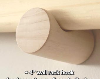 Puede incluir: Un gancho de pared de madera de color claro con forma cilíndrica, que presenta una muesca curva para el montaje. El texto en la imagen dice: ~ 4" wall rack hook for decorative surfboards display. El gancho tiene un acabado liso de veta natural.