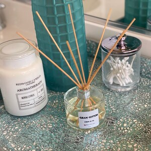 Może przedstawiać: Ozdobna taca zawiera świecę, dyfuzor patyczkowy i szklany słoik z patyczkami kosmetycznymi. Świeca jest oznaczona jako "Redwood Candles Aromatherapy Neroli Citrus". Dyfuzor jest oznaczony jako "Clean Cotton".