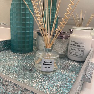 May include: A teal and silver mosaic patterned bathroom tray displays a reed diffuser, a candle, and a glass vase. The reed diffuser is labelled "Sparkling Grapefruit". The candle is labelled "Neroli Citrus". The tray is a decorative item.