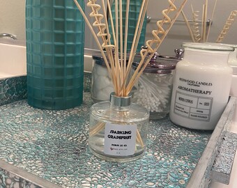 Könnte beinhalten: Ein dekoratives Badezimmer-Tablett mit einem türkisfarbenen und silbernen Mosaikmuster enthält einen Schilf-Diffusor, eine Kerze und eine Glasvase. Der Schilf-Diffusor trägt die Aufschrift "Sparkling Grapefruit". Die Kerze ist mit "Neroli Citrus" beschriftet.