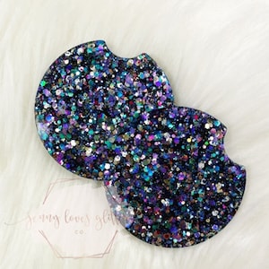 May include: Two round black coasters with a glittery finish. The glitter is a mix of iridescent blue, purple, and green.