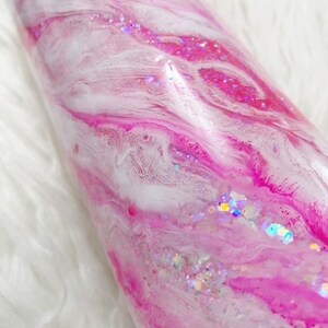 May include: A pink and white tumbler with a swirl design and iridescent glitter.