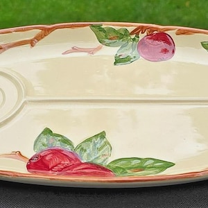 Può includere: Piatto da portata ovale con superficie color crema, diviso in sezioni. Presenta un disegno dipinto di mele rosse, foglie verdi e rami marroni. Il bordo è delineato in color marrone rossiccio.