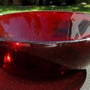 Puede incluir: Un cuenco de vidrio rojo oscuro con una superficie lisa y brillante. El cuenco está vacío y parece estar hecho de vidrio rojo rubí.