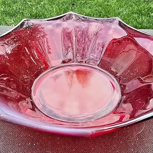May include: A red glass serving bowl with two handles. The bowl has a scalloped edge and a fluted design.