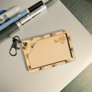 May include: A wooden rolling tray with a leaf design and the text "Roll Up" engraved on the surface. The tray is attached to a silver key chain.